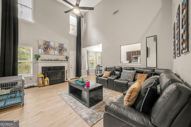 living room with plenty of natural light, ceiling fan, a high ceiling, and light hardwood / wood-style flooring