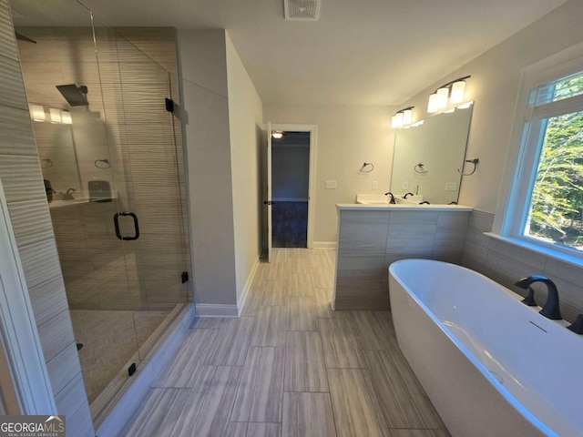 bathroom featuring plus walk in shower, vanity, and tile walls