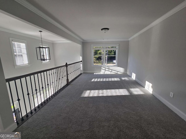 spare room featuring dark colored carpet, crown molding, and an inviting chandelier