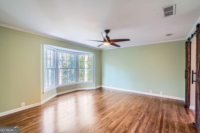 unfurnished room featuring dark hardwood / wood-style flooring, a barn door, ceiling fan, and ornamental molding