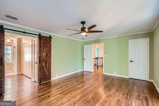 interior space with hardwood / wood-style flooring, ceiling fan, a barn door, and crown molding