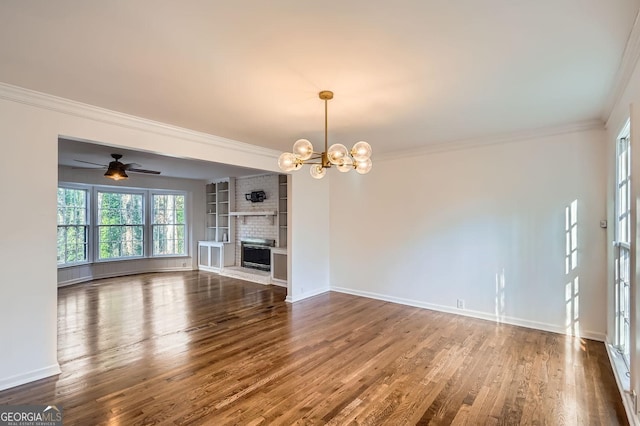 unfurnished living room with ceiling fan with notable chandelier, hardwood / wood-style flooring, a brick fireplace, and crown molding