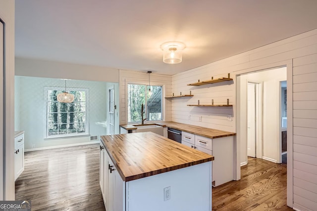 kitchen with wood counters, decorative light fixtures, a center island, white cabinetry, and wood walls