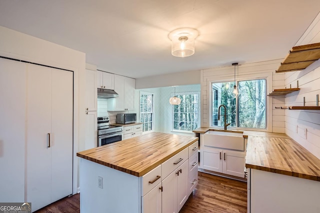 kitchen with sink, electric range, white cabinetry, hanging light fixtures, and butcher block counters