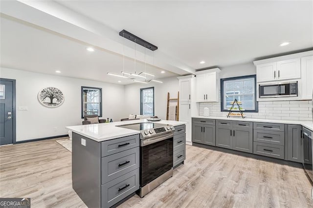 kitchen featuring stainless steel electric stove, built in microwave, tasteful backsplash, decorative light fixtures, and white cabinetry