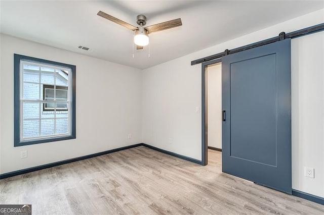 unfurnished room featuring ceiling fan, a barn door, and light wood-type flooring