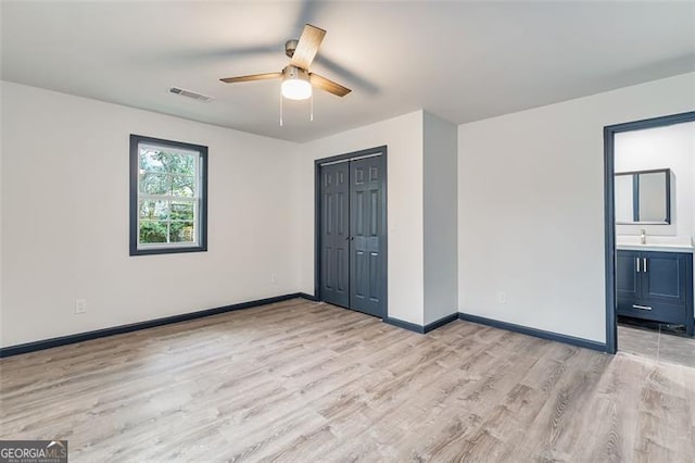 unfurnished bedroom featuring light wood-type flooring, ensuite bathroom, ceiling fan, sink, and a closet