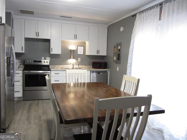 kitchen featuring appliances with stainless steel finishes, light stone counters, sink, wood-type flooring, and white cabinetry