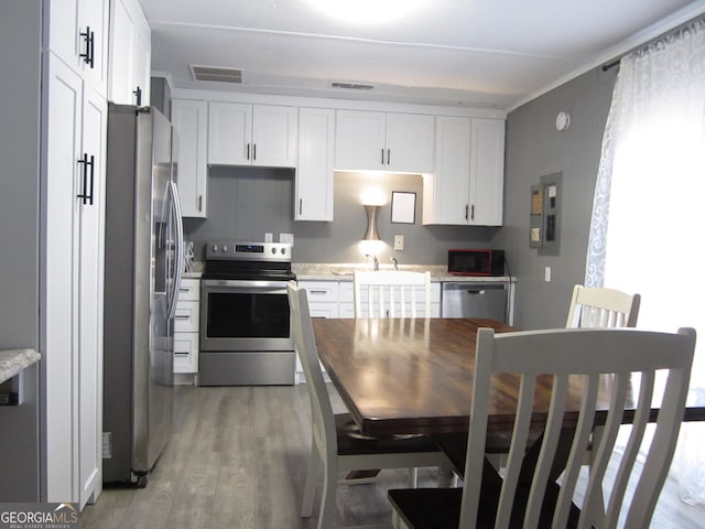 kitchen with light stone countertops, white cabinetry, wood-type flooring, and appliances with stainless steel finishes