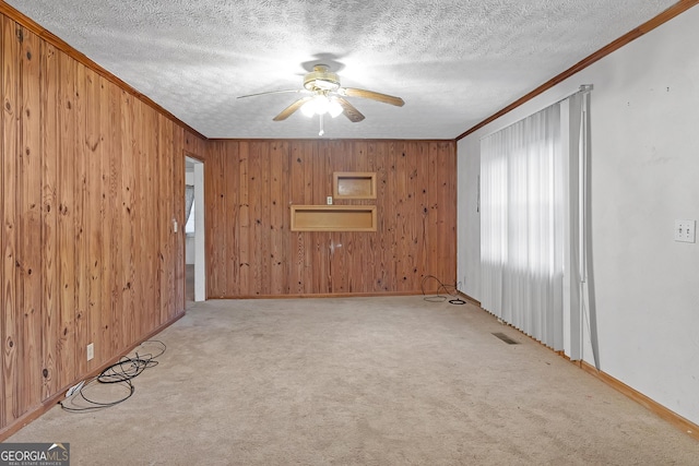 spare room with ceiling fan, light colored carpet, ornamental molding, and a textured ceiling