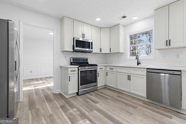 kitchen with white cabinetry, sink, light hardwood / wood-style flooring, and appliances with stainless steel finishes