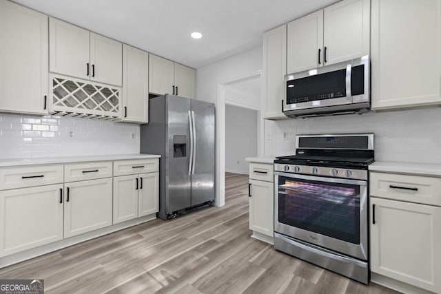 kitchen with backsplash, light hardwood / wood-style flooring, white cabinets, and stainless steel appliances