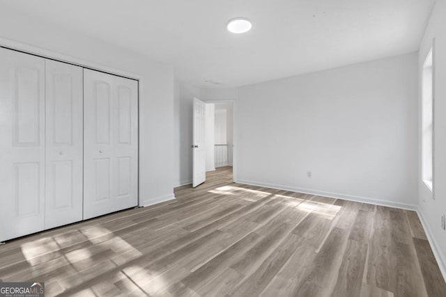 unfurnished bedroom with light hardwood / wood-style floors, multiple windows, and a closet