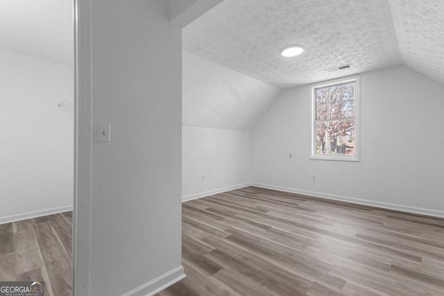 additional living space featuring vaulted ceiling, light hardwood / wood-style flooring, and a textured ceiling