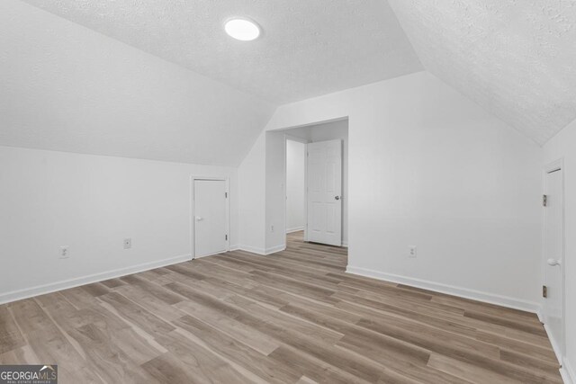 bonus room featuring light wood-type flooring, a textured ceiling, and vaulted ceiling