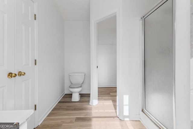 bathroom with hardwood / wood-style flooring, toilet, and a shower with door