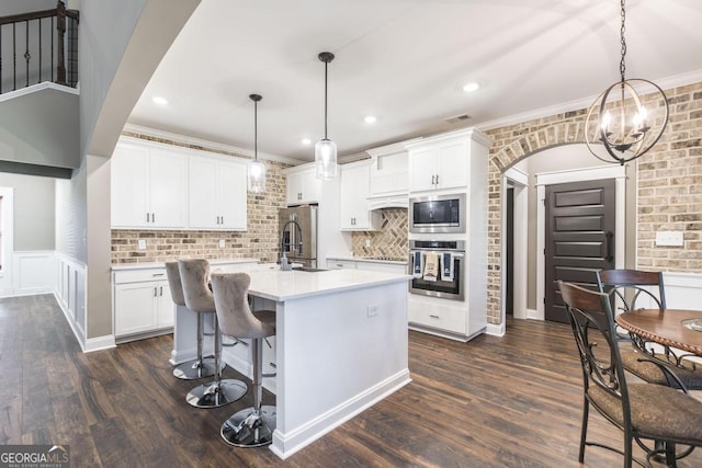 kitchen with arched walkways, white cabinetry, light countertops, appliances with stainless steel finishes, and hanging light fixtures