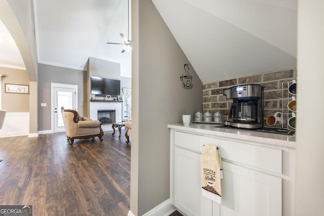 bar featuring baseboards, decorative backsplash, dark wood-style floors, vaulted ceiling, and a fireplace