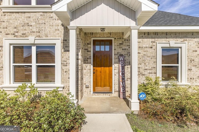 property entrance featuring a shingled roof, board and batten siding, and brick siding