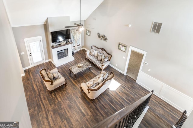 living room featuring high vaulted ceiling, a decorative wall, visible vents, dark wood-style floors, and a glass covered fireplace