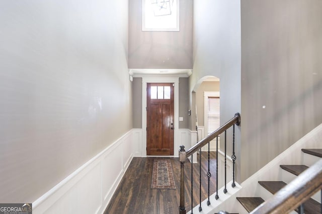 foyer entrance featuring arched walkways, a decorative wall, stairway, wainscoting, and dark wood-style floors