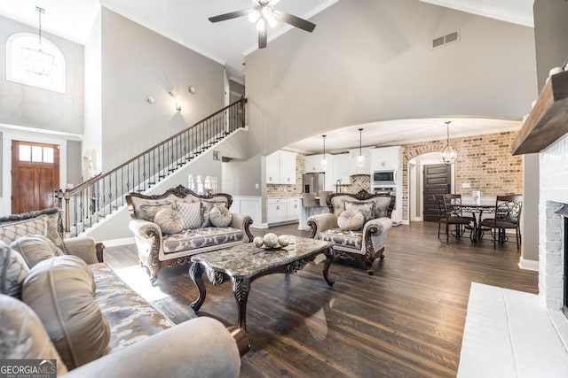 living room featuring arched walkways, ceiling fan with notable chandelier, dark wood-type flooring, visible vents, and stairs