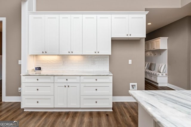 kitchen with white cabinets, backsplash, light stone countertops, and dark wood-type flooring