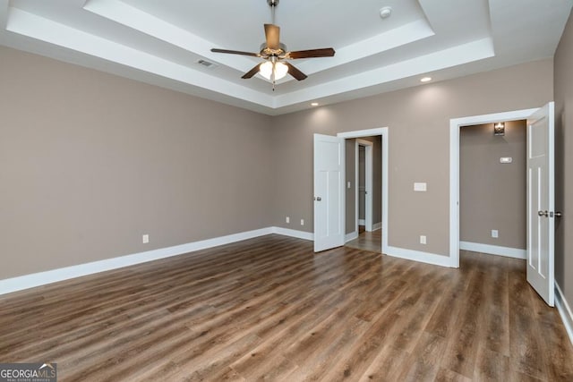 unfurnished bedroom with dark hardwood / wood-style floors, a raised ceiling, and ceiling fan