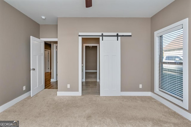 unfurnished bedroom with a barn door, a closet, ceiling fan, and light colored carpet