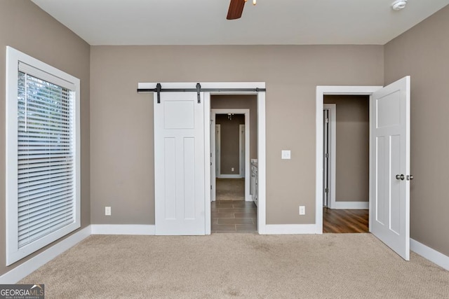 unfurnished bedroom featuring carpet flooring, ceiling fan, and a barn door