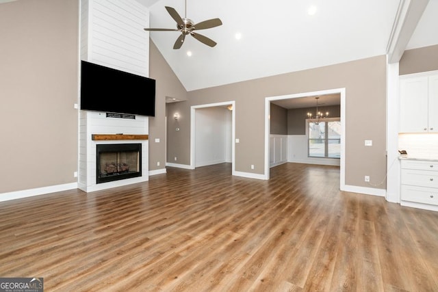 unfurnished living room featuring ceiling fan with notable chandelier, light wood-type flooring, a fireplace, and high vaulted ceiling