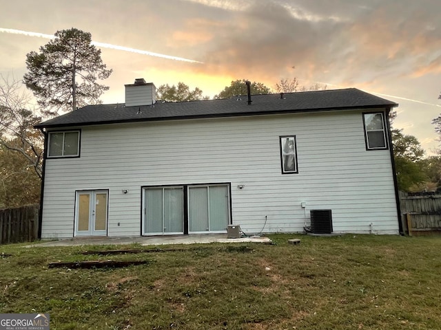 back house at dusk with a lawn and central AC