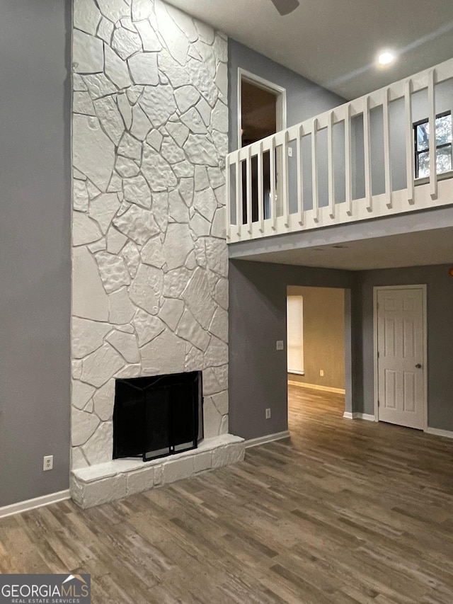 unfurnished living room with a high ceiling, hardwood / wood-style flooring, and a stone fireplace