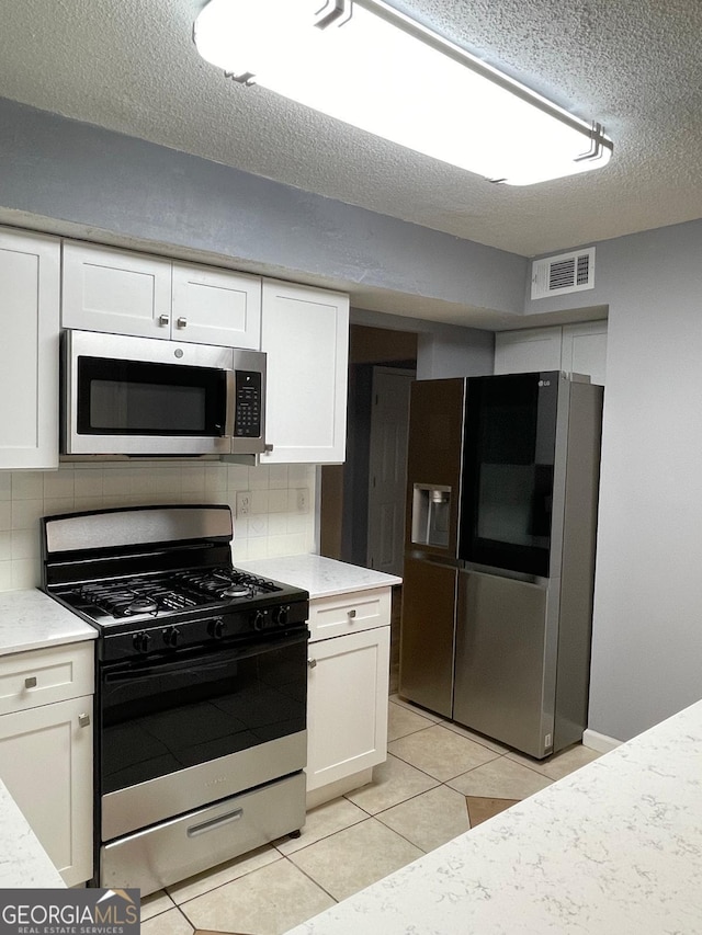 kitchen with light tile patterned floors, a textured ceiling, appliances with stainless steel finishes, and tasteful backsplash