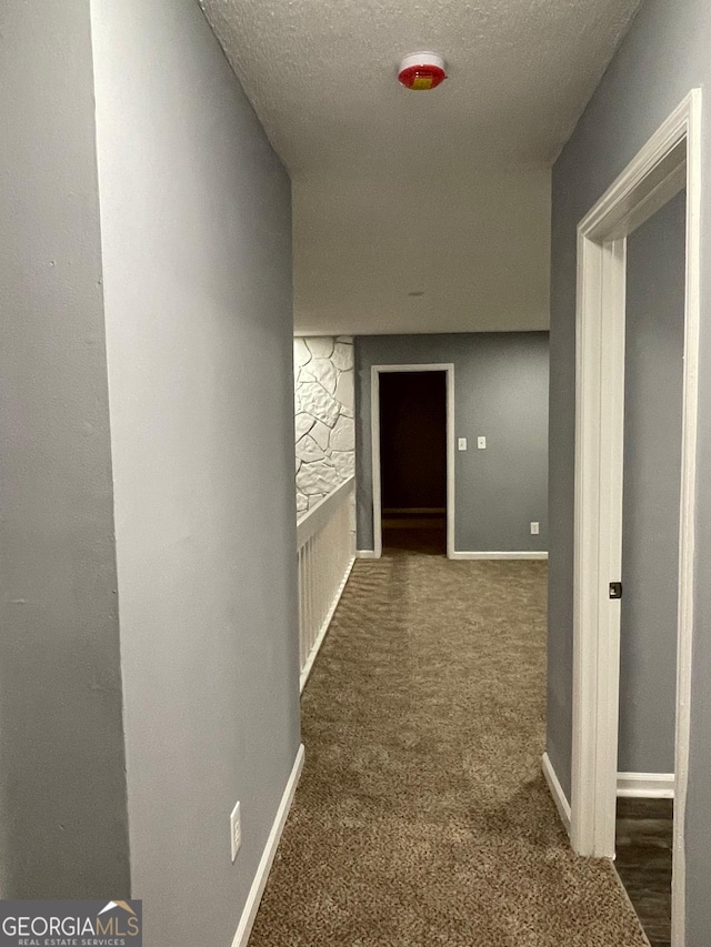 hallway featuring dark colored carpet and a textured ceiling