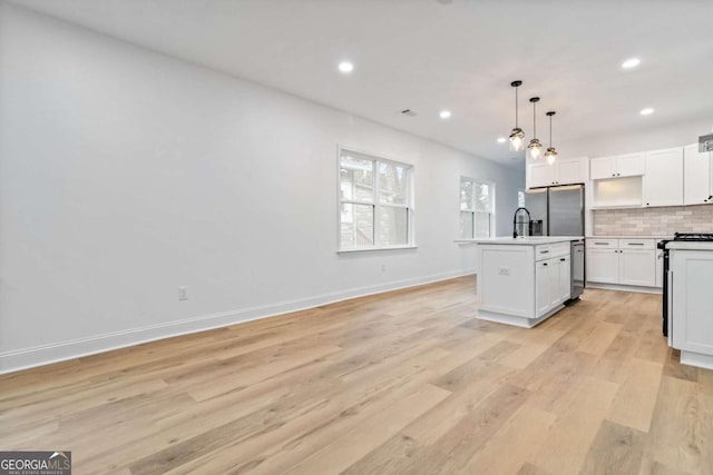 kitchen featuring white cabinetry, tasteful backsplash, an island with sink, pendant lighting, and appliances with stainless steel finishes