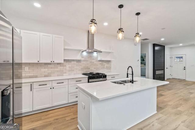 kitchen featuring white cabinetry, stainless steel gas stove, sink, hanging light fixtures, and a kitchen island with sink