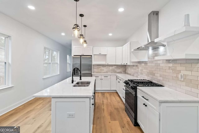 kitchen featuring stainless steel appliances, wall chimney range hood, pendant lighting, a center island with sink, and white cabinets