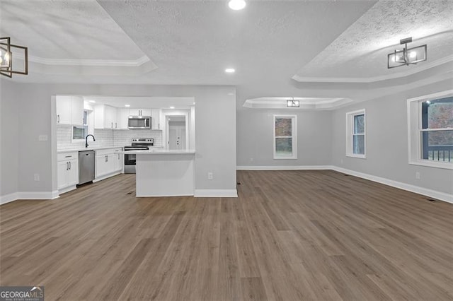 kitchen with white cabinets, appliances with stainless steel finishes, dark hardwood / wood-style flooring, and a tray ceiling