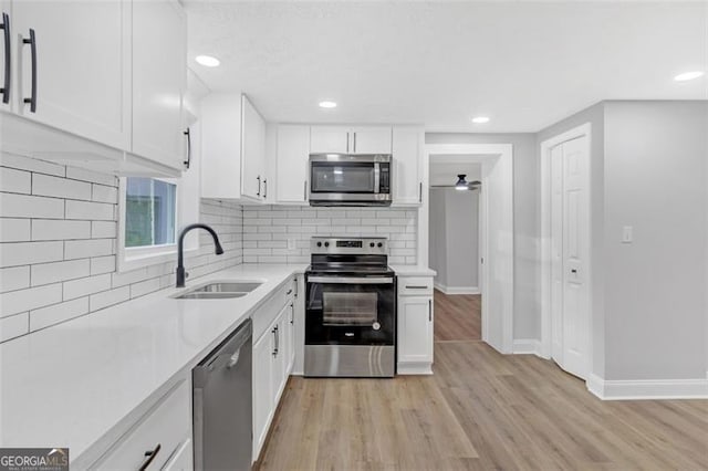 kitchen featuring backsplash, sink, light hardwood / wood-style flooring, white cabinetry, and stainless steel appliances