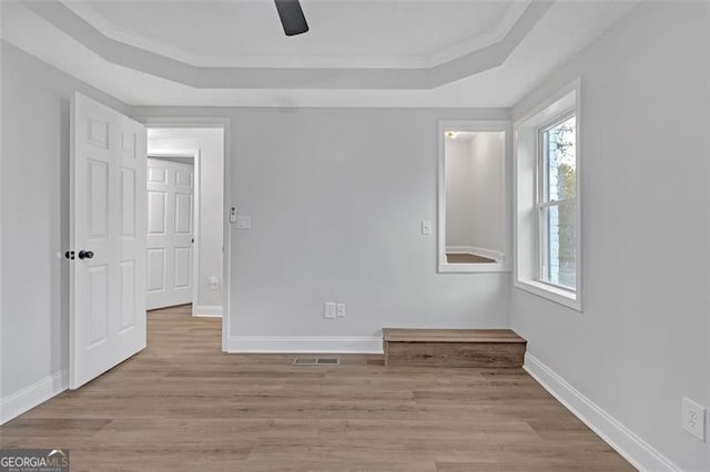 spare room featuring a tray ceiling, crown molding, and light hardwood / wood-style floors