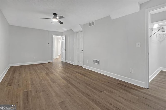 unfurnished bedroom featuring a closet, a walk in closet, ceiling fan, and dark hardwood / wood-style flooring