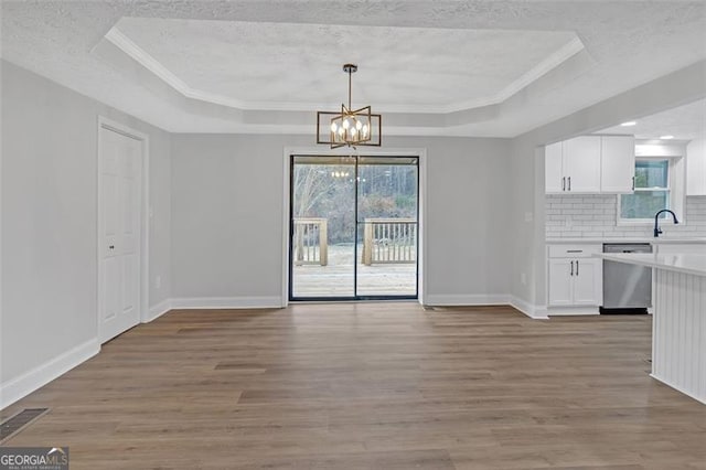 unfurnished dining area with a tray ceiling, a chandelier, crown molding, and light hardwood / wood-style floors