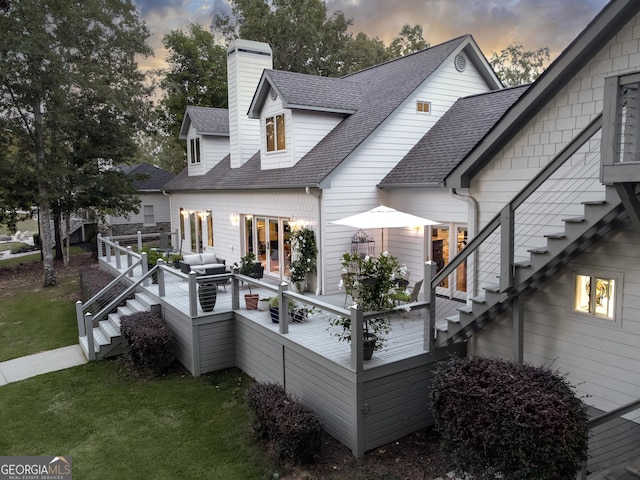 back house at dusk featuring a lawn, an outdoor hangout area, and a deck