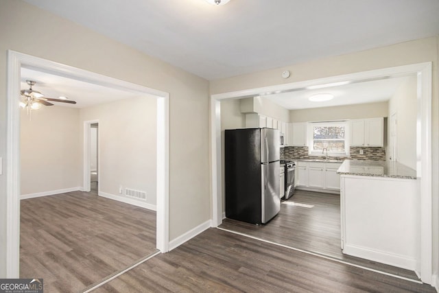 kitchen with white cabinetry, dark wood-type flooring, stainless steel appliances, tasteful backsplash, and light stone counters