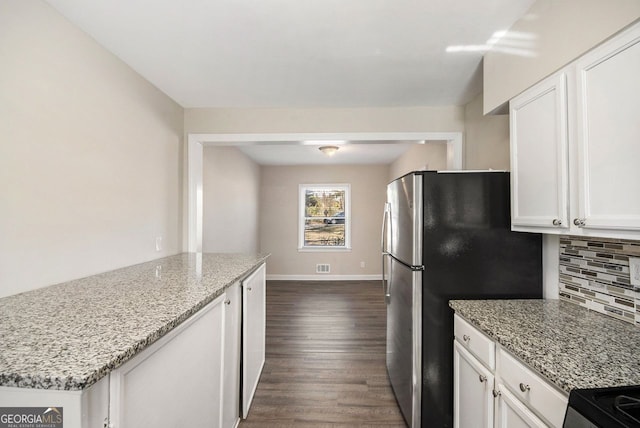 kitchen with white cabinets, decorative backsplash, stainless steel fridge, light stone counters, and dark hardwood / wood-style flooring