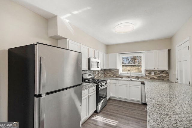 kitchen featuring backsplash, white cabinets, sink, light stone countertops, and appliances with stainless steel finishes