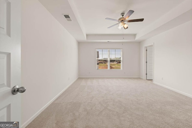 carpeted empty room with ceiling fan and a raised ceiling