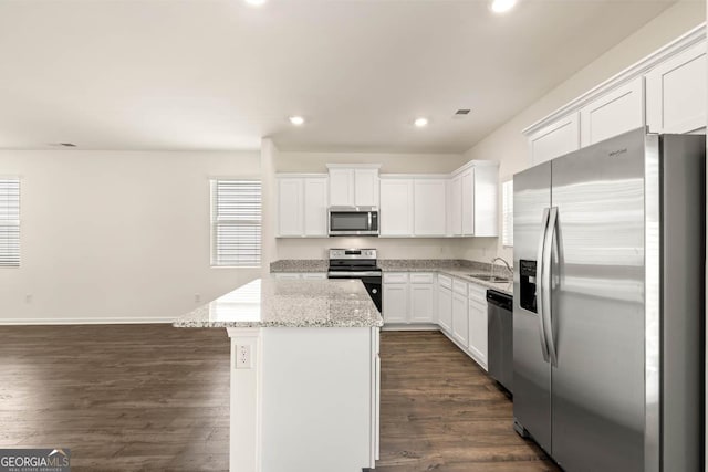 kitchen featuring appliances with stainless steel finishes, light stone counters, sink, a center island, and white cabinetry