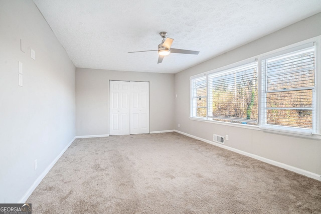 unfurnished bedroom featuring a textured ceiling, carpet floors, a closet, and ceiling fan